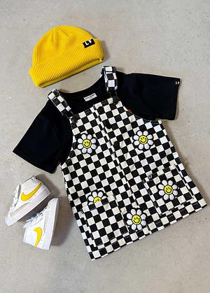 Children's outfit with black t-shirt, Little Trouble Little Bloomer Checker Corduroy Dress, yellow beanie, and sneakers on a gray surface