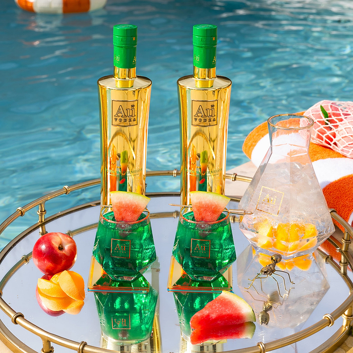 Two Au Vodka Watermelon bottles and cocktails on a mirrored tray by a pool