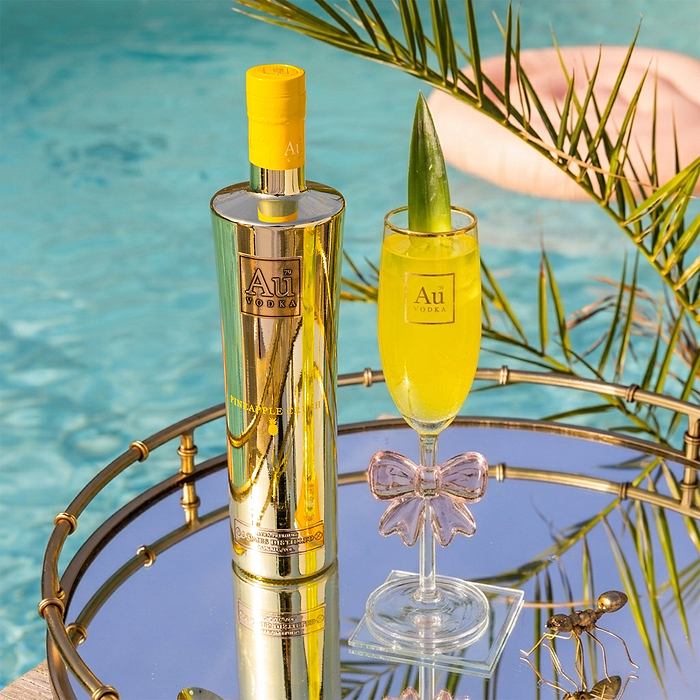 Au Vodka Pineapple Crush bottle and cocktail on a mirrored tray by a pool