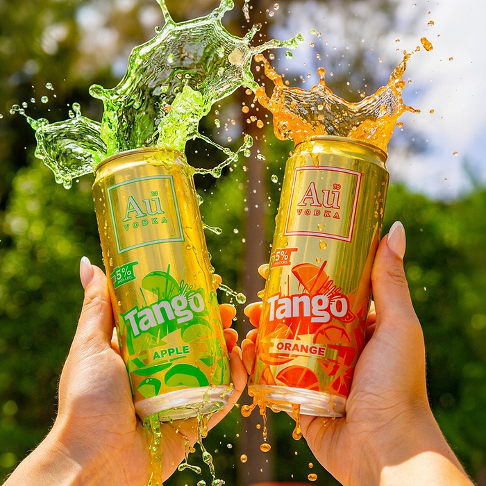 Hands holding two Au Vodka Tango cans, apple and orange, with liquid splashing from the tops