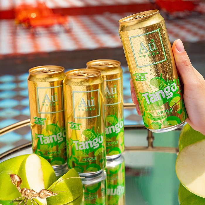 Hand holding a cold Au Vodka Tango Apple can, with three more cans and sliced green apples on a reflective surface