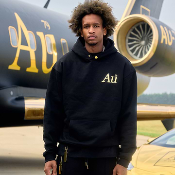 Man wearing a black hoodie with 'Au' logo in front of an airplane