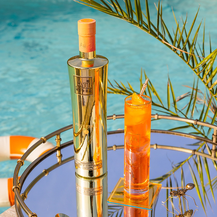Au Vodka Juicy Peach bottle and cocktail on a mirrored tray by a pool