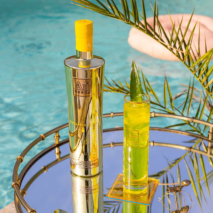 Au Vodka Pineapple Crush bottle and cocktail on a mirrored tray by a swimming pool