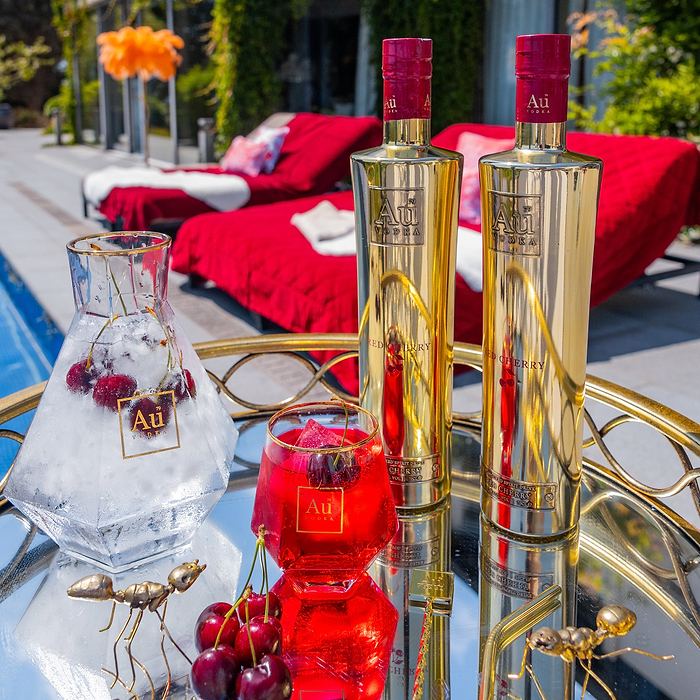 Au Vodka Red Cherry bottles, carafe with cherries and ice, and a cocktail on a gold tray