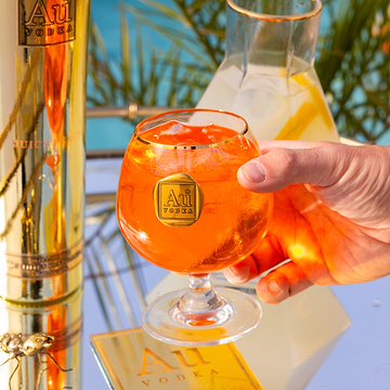 Hand holding an Au Vodka branded glass filled with an orange cocktail