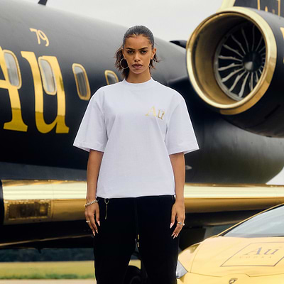 Person wearing a white t-shirt with gold logo in front of a black and gold airplane