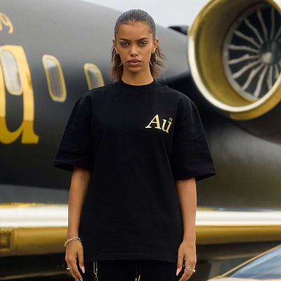 Person wearing a black t-shirt with 'Au' logo in front of an airplane