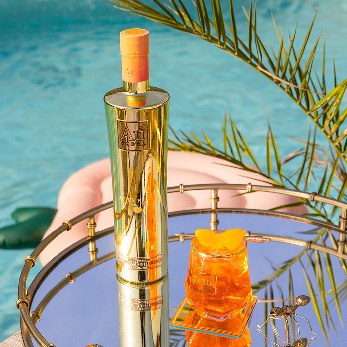 Au Vodka Juicy Peach bottle and cocktail on a mirrored tray by a pool