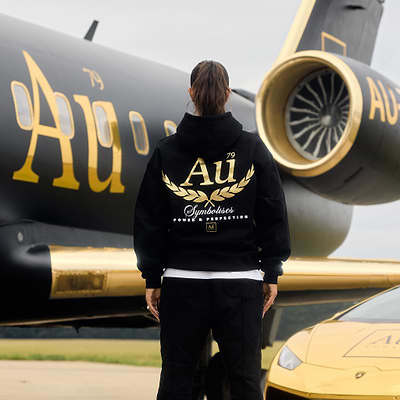 Person wearing a black hoodie with gold 'Au' logo on the back in front of car