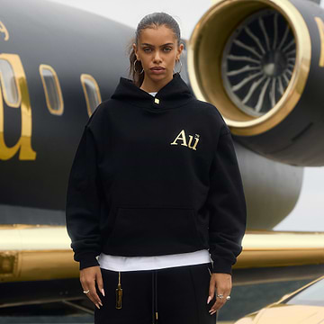 Person wearing a black hoodie with gold 'Au' lettering in front of a luxury airplane.
