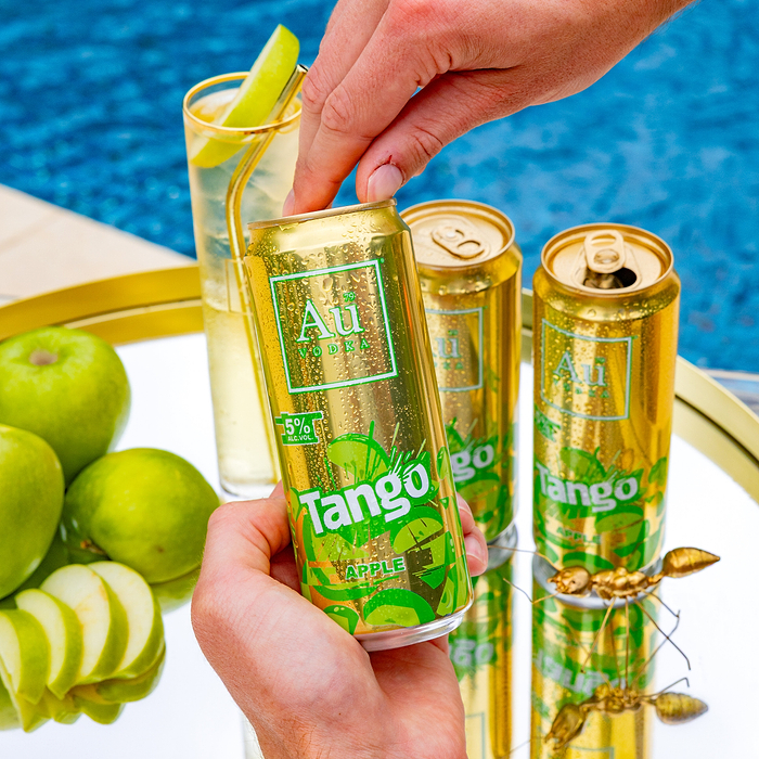 Hand holding a gold Au Vodka Tango Apple can with water droplets, next to two other cans and green apples