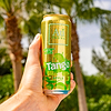 Hand holding a cold Au Vodka Tango Apple can with condensation, palm trees in the background