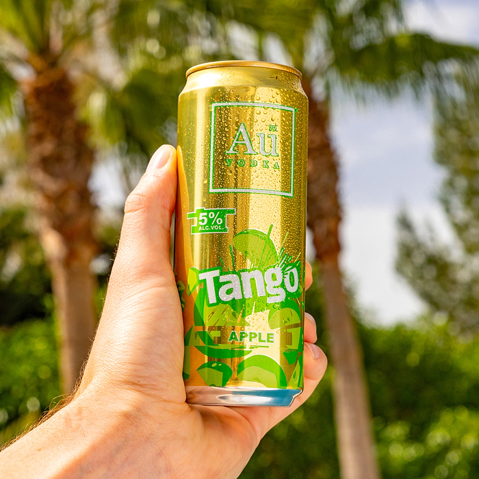 Hand holding a cold Au Vodka Tango Apple can with condensation, palm trees in the background
