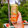 Hand holding a cold, wet can of Au Vodka Tango Orange against a blurred green background