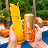 Hands holding an Au Vodka Tango Orange can and a tall glass of orange drink by a pool