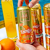 Hand holding a cold Au Vodka Tango Orange can with water droplets, next to other cans and a glass of orange drink