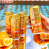 Hand holding a gold Au Vodka Tango Orange can, with three more cans on a mirrored tray with oranges