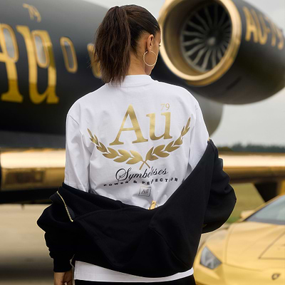 Person wearing a white t-shirt with gold "Au" text in front of an airplane
