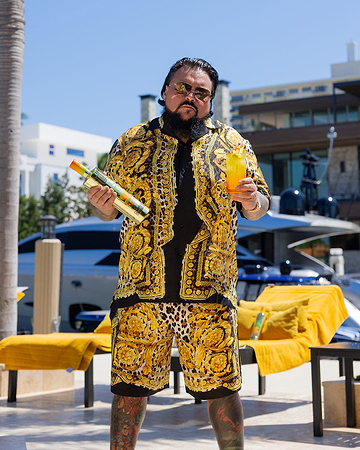 Man in Versace shirt and shorts holding a bottle of Villon and a cocktail