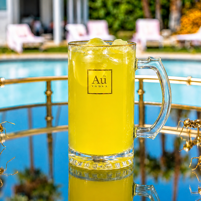 Au Vodka cocktail in a glass mug with ice on a reflective surface by a swimming pool