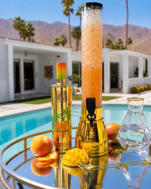 Au Vodka Miami Mango bottle and drink dispenser with fresh fruit on a tray by a pool