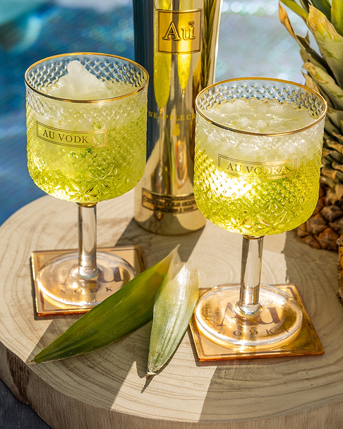 Two Au Vodka Crystal Cocktail Glasses cocktails with a gold bottle of Au Vodka and a pineapple leaves