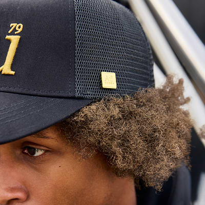 Close-up of person wearing a black hat with gold accents and a logo.