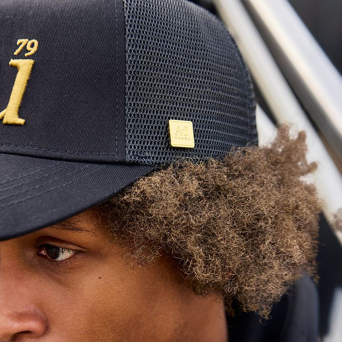 Close-up of person wearing a black hat with gold accents and a logo.