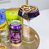Au Vodka cocktail in a purple glass with dried lemon slices, next to a can of KA Black Grape