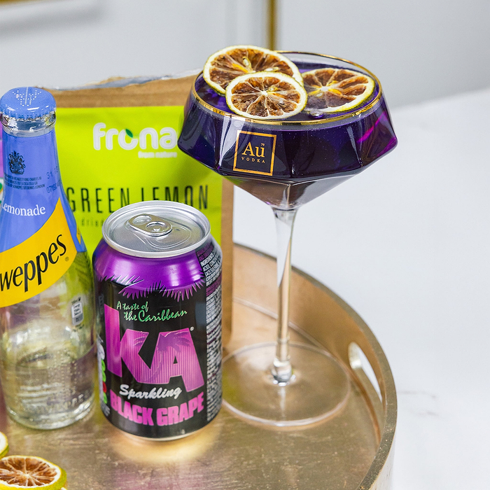 Au Vodka cocktail in a purple glass with dried lemon slices, next to a can of KA Black Grape