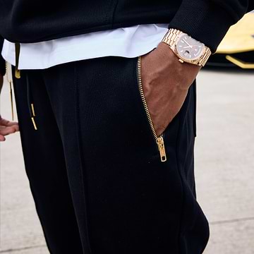 Person wearing black joggers with gold zip pockets