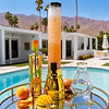 Au Vodka Miami Mango bottle next to a tall drink dispenser and glass carafe on a poolside tray