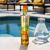 Au Vodka Miami Mango bottle and a clear decanter by a pool