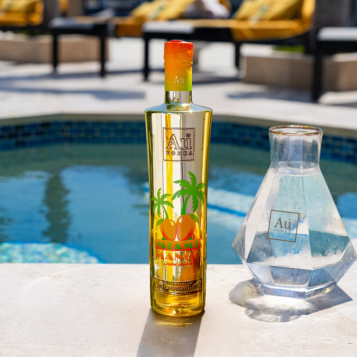 Au Vodka Miami Mango bottle and a clear decanter by a pool