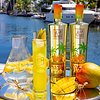 Au Vodka Miami Mango bottles, cocktail, and fresh mango on a silver tray by a canal