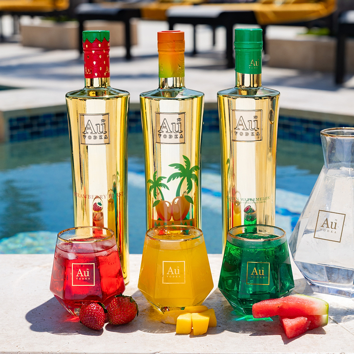 Three Au Vodka bottles and three glasses of vodka cocktails with fruit by a pool