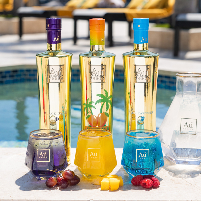 Three Au Vodka bottles and three glasses of vodka cocktails with fruit by a pool