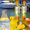 Au Vodka Miami Mango bottles, cocktail, and fresh mango on a mirrored tray with a yacht in background