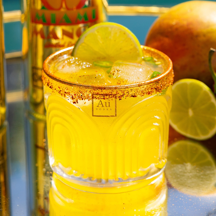 Au Vodka mango cocktail with a lime wedge and chili salt rim