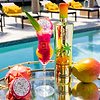 Au Vodka Miami Mango bottle, dragon fruit, mango, and a cocktail on a reflective tray by a pool