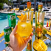 Hand holding a diamond cut glass of Au Vodka Mango Breeze cocktail with mango slices, Sprite cans, and Au Vodka bottles