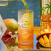 Au Vodka Miami Mango being poured into a glass with ice, next to a mango and a bottle