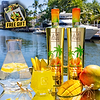 Two Au Vodka Miami Mango bottles, mango slices, and a drink on a reflective surface by a canal