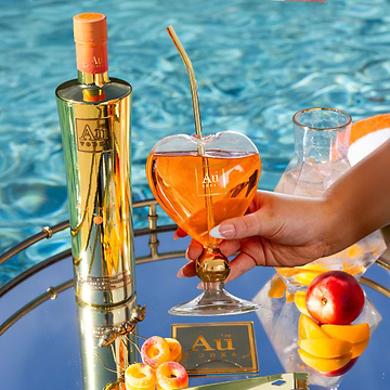 Au Vodka bottle and heart-shaped glass with a drink, on a mirrored tray by a pool