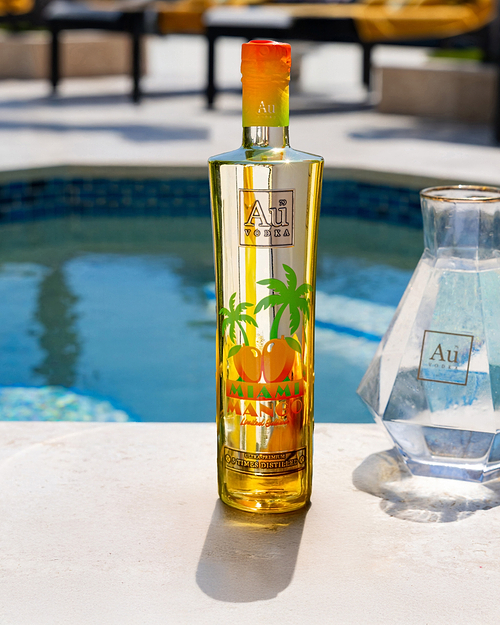Au Vodka Miami Mango bottle next to a pool with a clear Au Vodka decanter