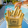 Hand holding an Au Vodka Black Grape can over an ice bucket filled with various Au Vodka cans by a swimming pool