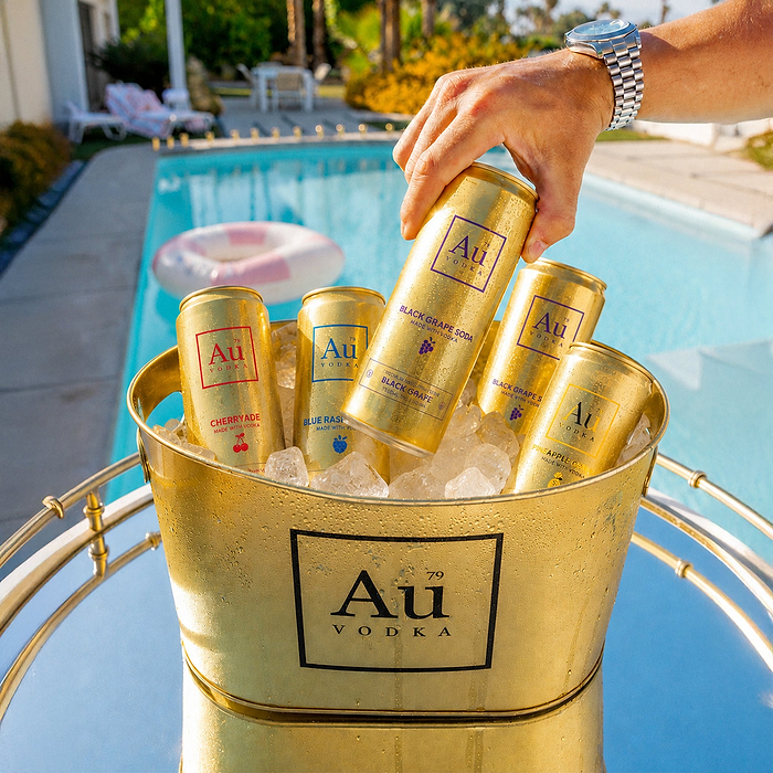 Hand holding an Au Vodka Black Grape can over an ice bucket filled with various Au Vodka cans by a swimming pool