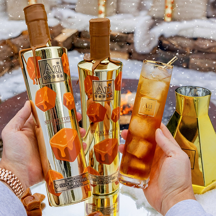 Two bottles of Au Vodka Sticky Toffee held by a person with a snowy background.