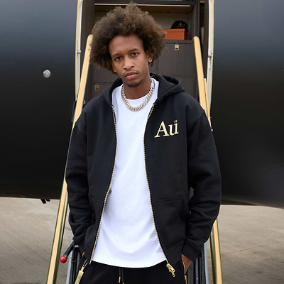 Person wearing a black hoodie with 'Au' logo in front of an airplane